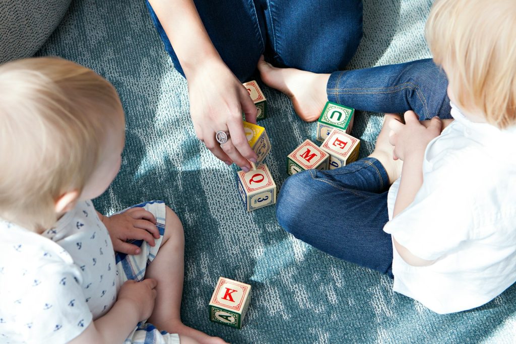 An adult and young children building with wooden letter blocks on the floor